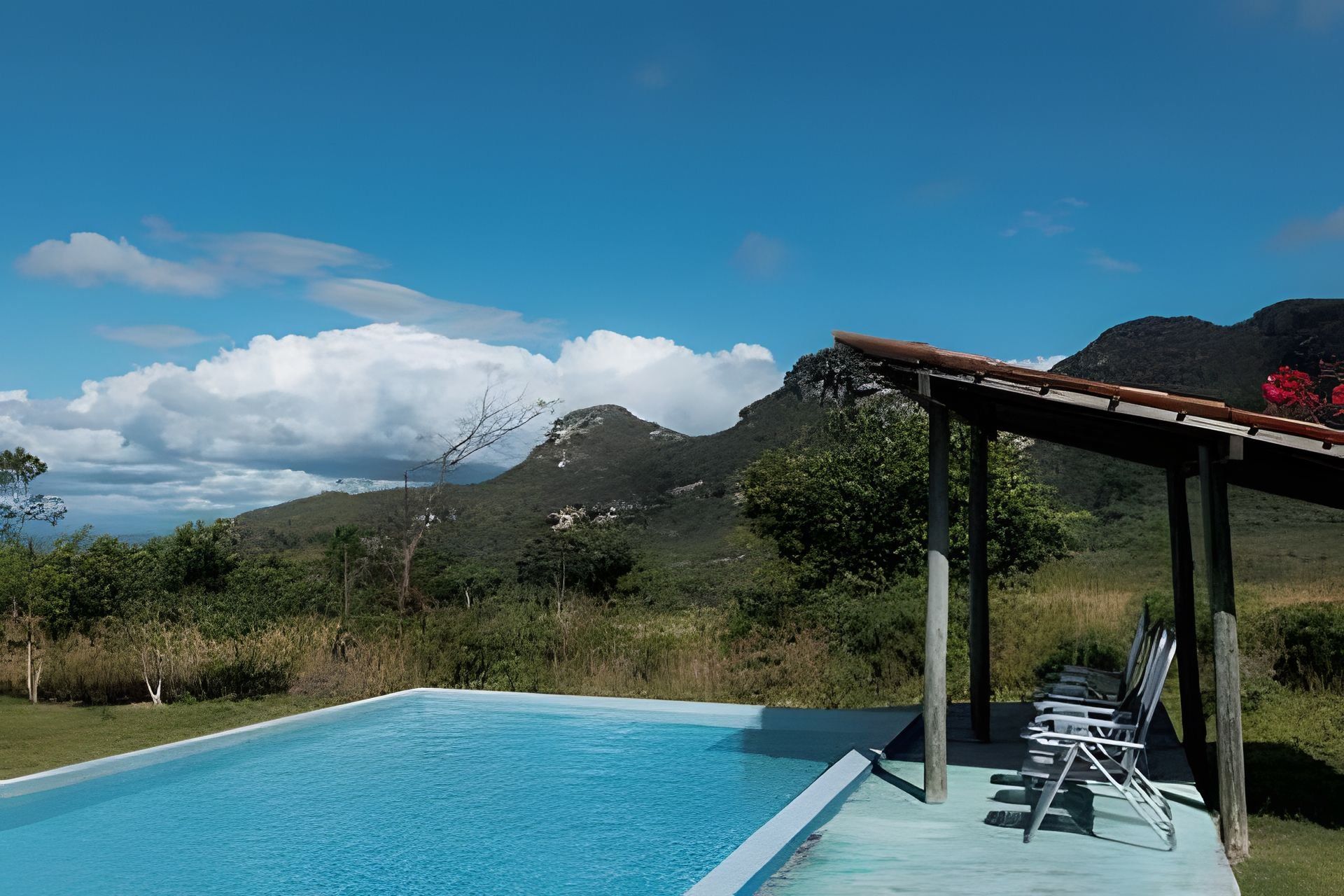 Una piscina con vistas a montañas, una zona de estar cubierta y un cielo despejado.