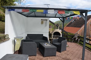 An outdoor seating area with wicker furniture, a pizza oven, and a view of a mountain. - Vacation Home Am Stein – Family Comfort in the Elbe Sandstone Mountains (Königstein)