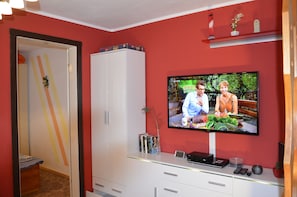 A room with a television mounted on the wall, a white cabinet, and a small shelf with decorative items. - Vacation Home Am Stein – Family Comfort in the Elbe Sandstone Mountains (Königstein)