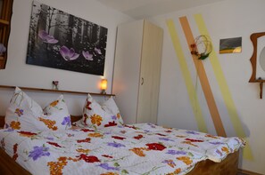 A bedroom with a bed, a nightstand, a wall-mounted lamp, a painting, and a mirror. - Vacation Home Am Stein – Family Comfort in the Elbe Sandstone Mountains (Königstein)