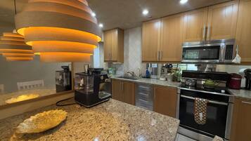 A modern kitchen with granite countertops, stainless steel appliances, wooden cabinets, and pendant lighting.