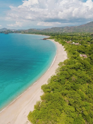 An aerial view of a coastal area with a sandy beach, dense greenery, and distant hills. - Casita Nimbú, A Peaceful Escape Close to Beaches (Cabo Velas)