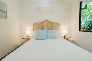 A hotel room with a large bed, two bedside tables with lamps, a ceiling air conditioner, and a window with a view of greenery. - Casita Nimbú, A Peaceful Escape Close to Beaches (Cabo Velas)