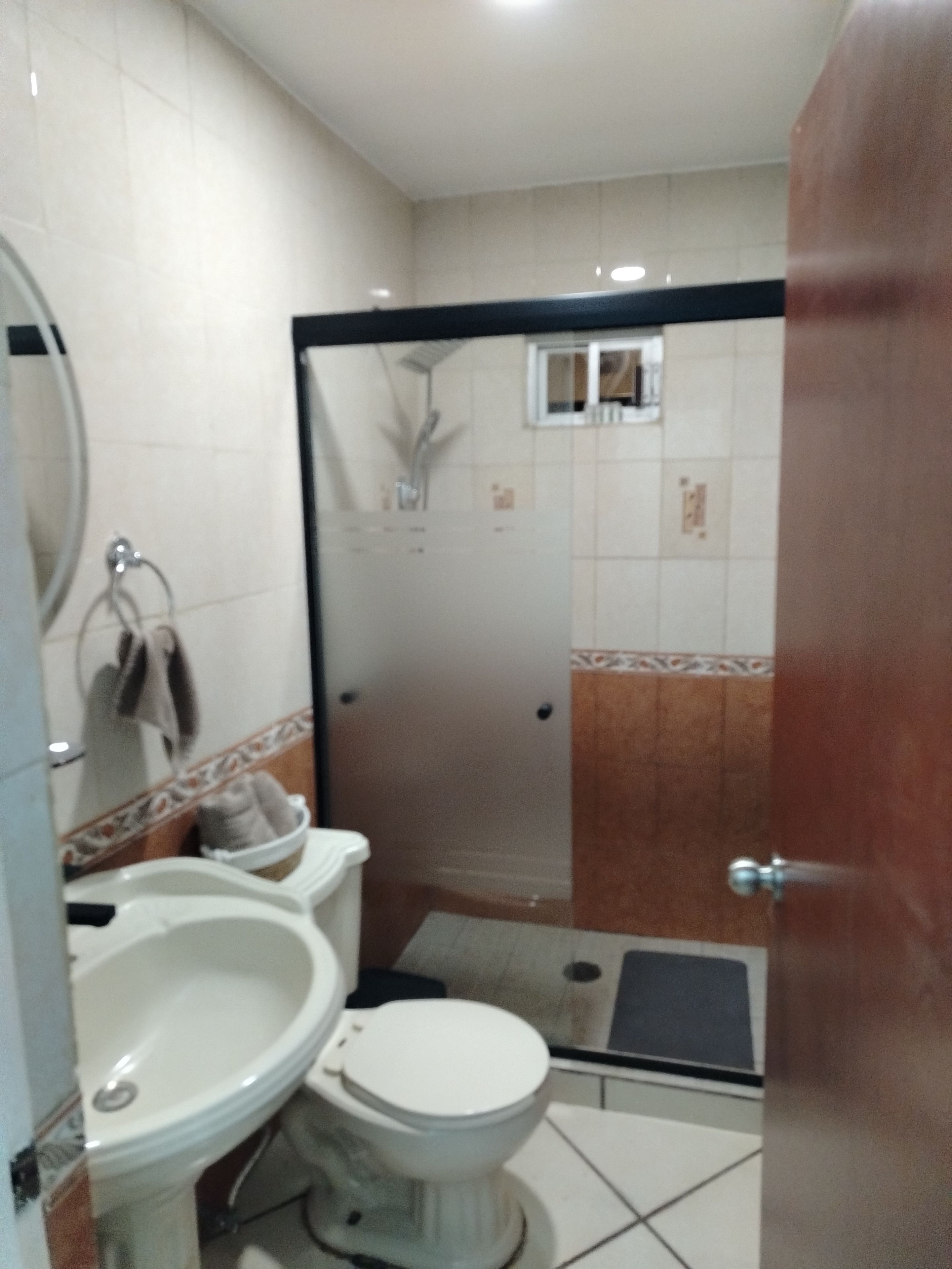 A bathroom with a toilet, bidet, and sink. There is a shower area with a glass door. The floor is tiled, and the walls have a decorative border.