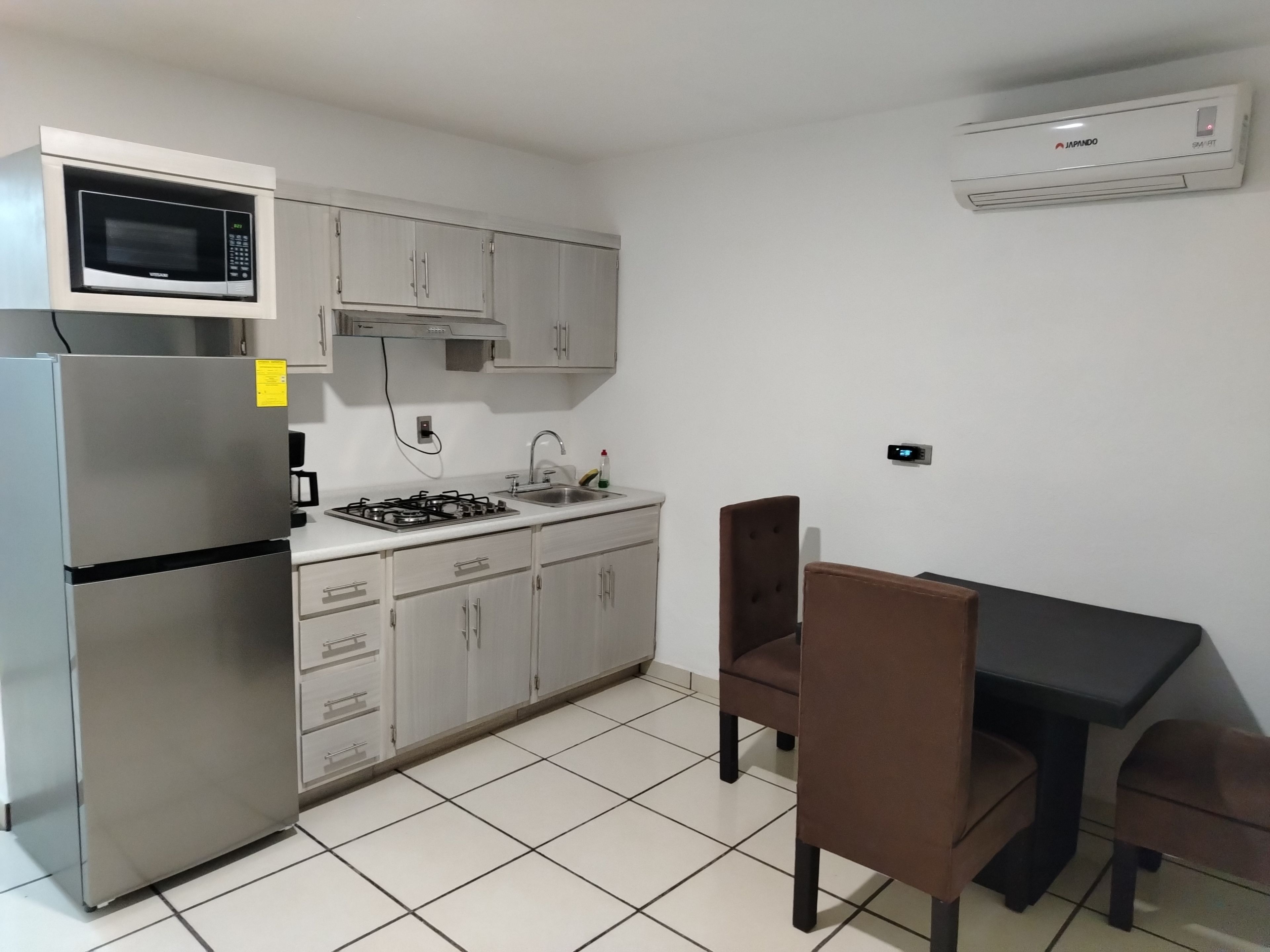 A kitchen with a microwave, stove, refrigerator, and cabinets. There is a dining table with chairs.