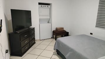 A bedroom with a bed, a television on a dresser, a washing machine, and a small stool.