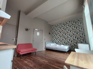Een kleine kamer met een bed, een rode stoel, een tafeltje en een behang met een patroon.