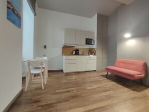 Een kamer met een houten vloer, een eettafel met stoelen, een kitchenette met kastjes en een roze bank.