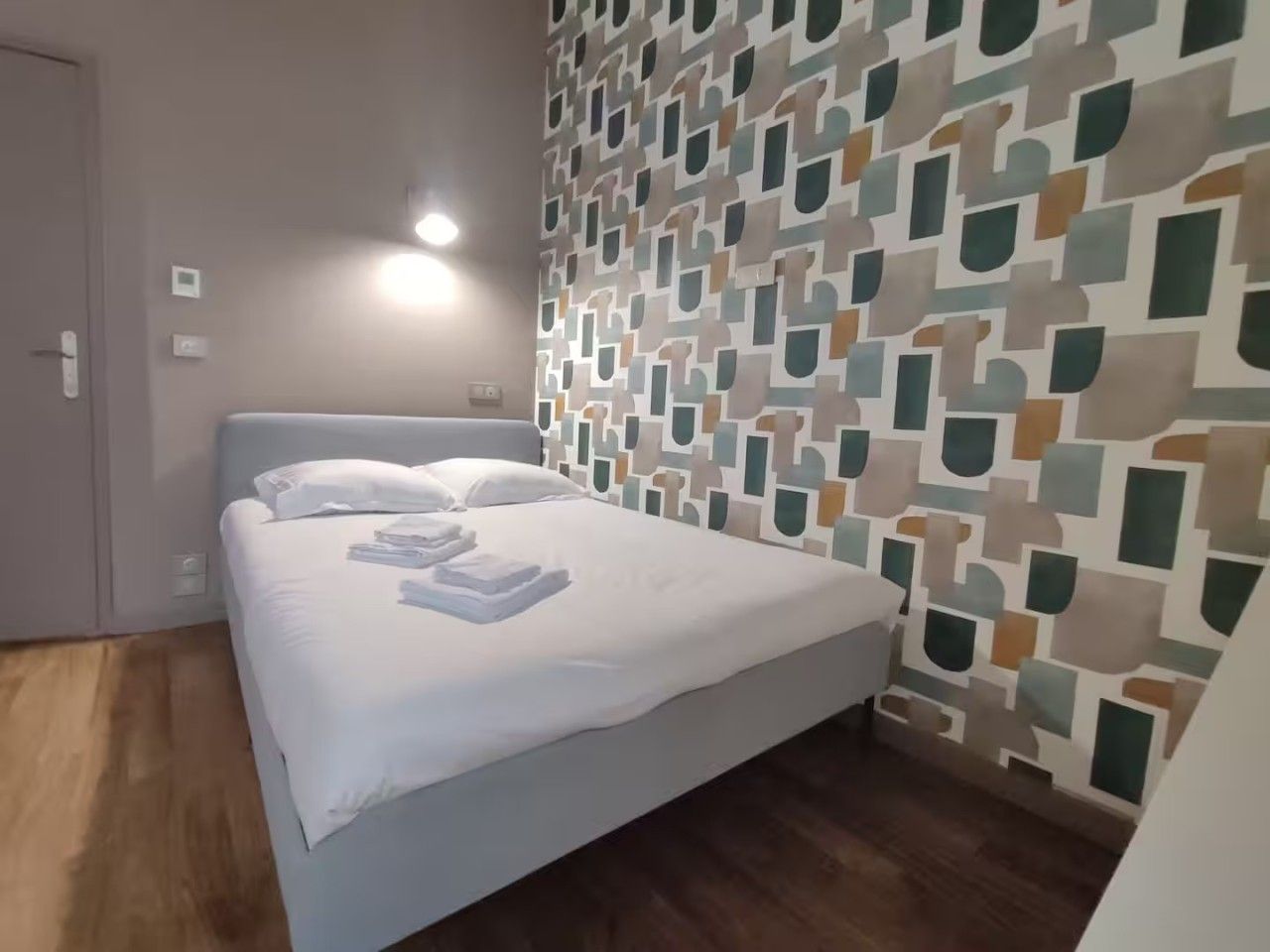 A hotel room with a bed, a patterned wall, and a wooden floor.