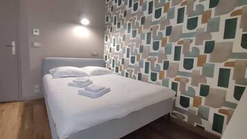 A hotel room with a bed, a patterned wall, and a wooden floor.