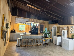 Una cocina rústica con paredes de madera, una isla central, taburetes de bar, un refrigerador, una lavadora y un ventanal con vistas.