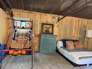 Una habitación con un aro de baloncesto, una cama, un aparador y un cuadro en la pared.