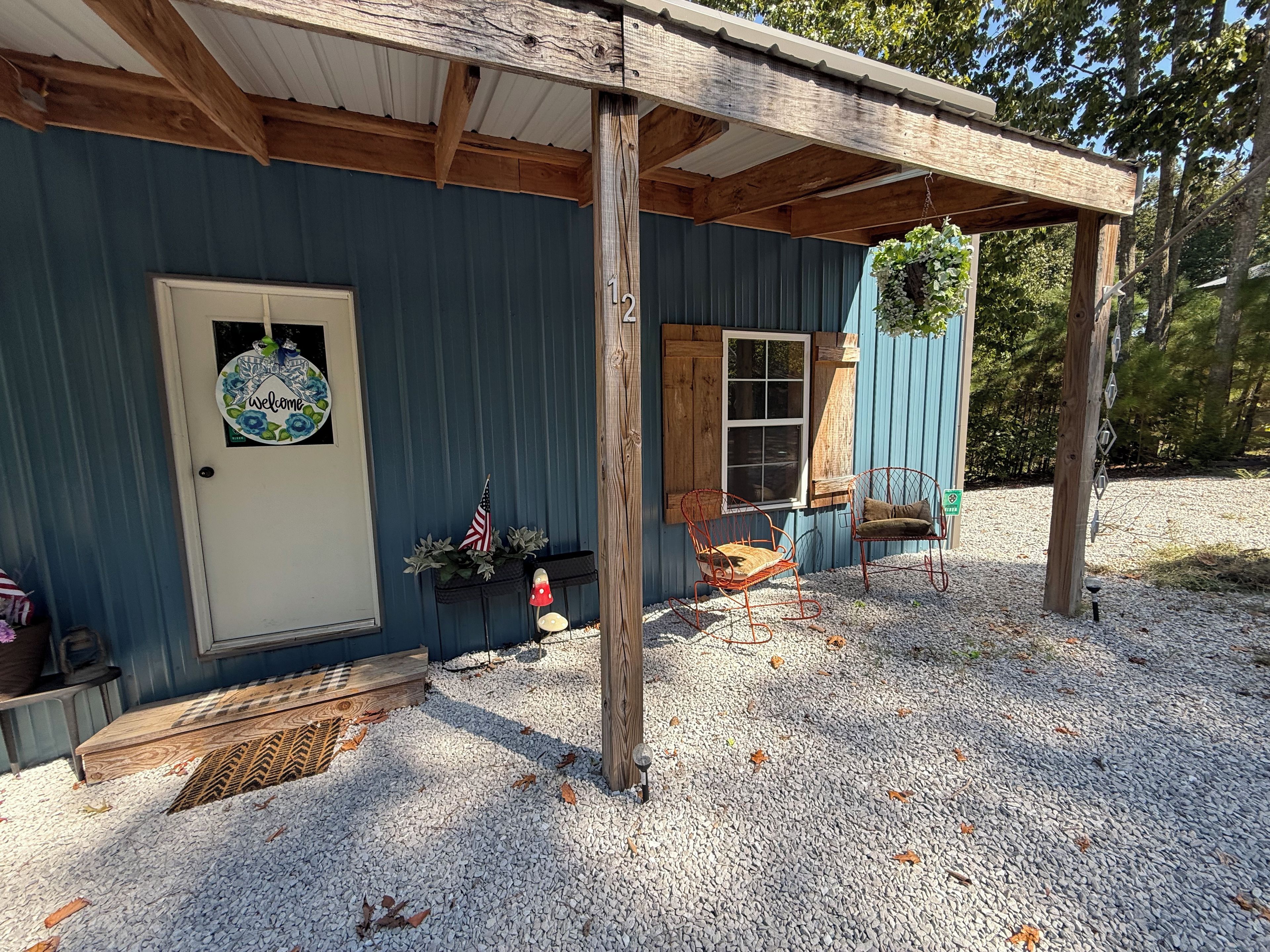 Een eenvoudige houten chalet met een terras, een bord met een welkomstboodschap, een kleine Amerikaanse vlag en een bank.