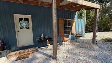 Een eenvoudige houten chalet met een terras, een bord met een welkomstboodschap, een kleine Amerikaanse vlag en een bank.