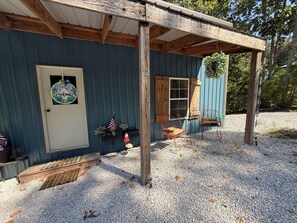 Een eenvoudige houten chalet met een terras, een bord met een welkomstboodschap, een kleine Amerikaanse vlag en een bank.