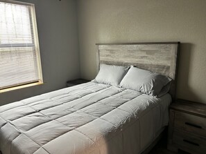 Una cama con cabecera, una mesita de noche y una ventana con persianas.