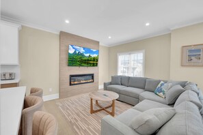 Ein modernes Wohnzimmer mit Flachbildfernseher an einer strukturierten Wand, Kamin, grauem Sofa und einem kleinen Holztisch.
