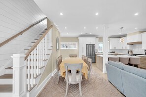 A modern kitchen with white cabinetry, a stainless steel refrigerator, and a dining area with a table and chairs. - Lavallette Beach House 4BR/3BA - Perfect for Fall Getaways! - Sleeps 10 - Unit A (Lavallette)