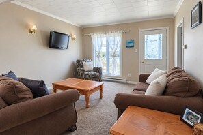 A living room with two sofas, a coffee table, a TV mounted on the wall, and a door with a window. - Rest Easy in Dildo | By the Sea | South Dildo (South Dildo)