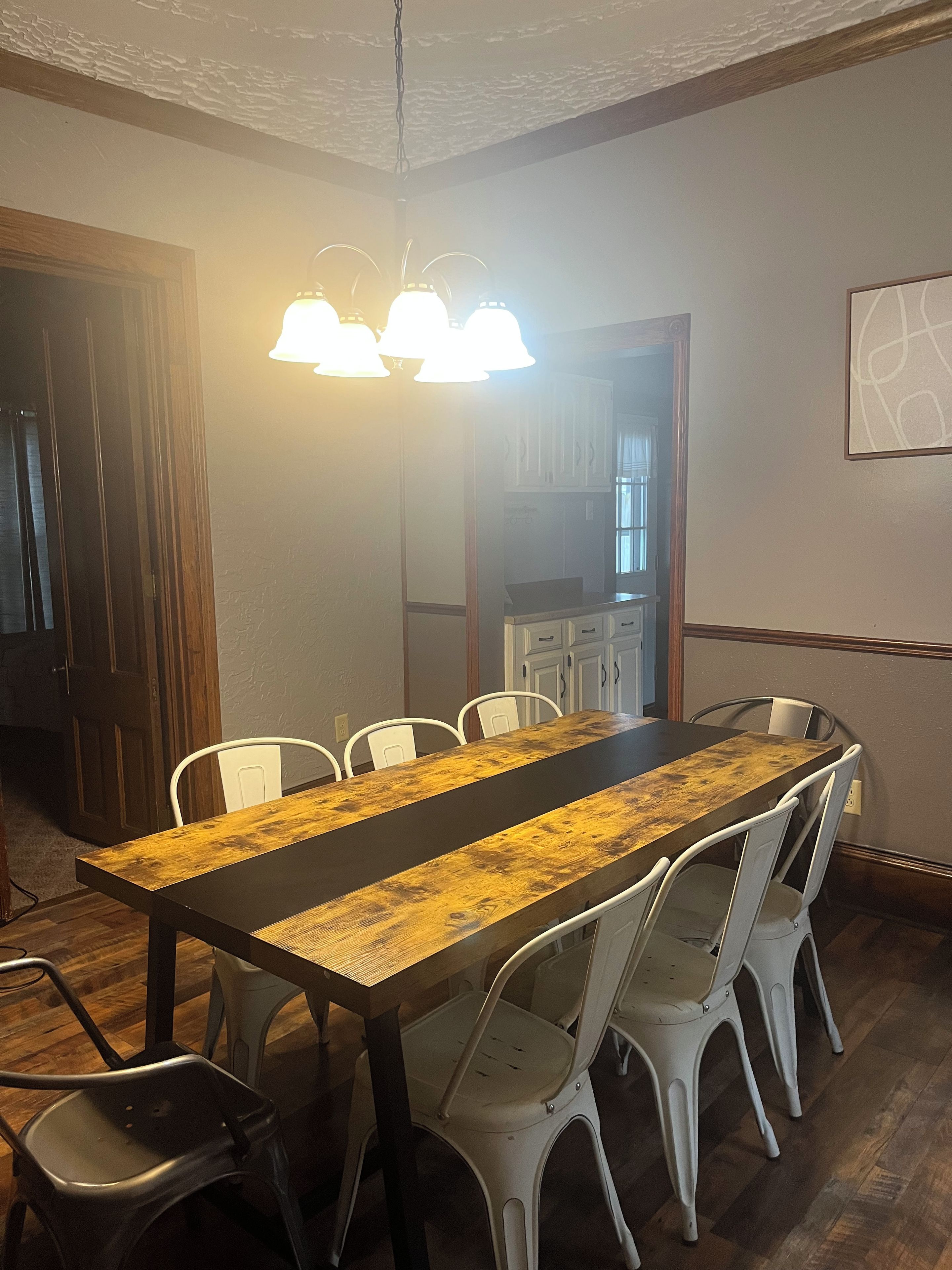 Un espace repas avec une longue table en bois, des chaises blanches et un luminaire suspendu.