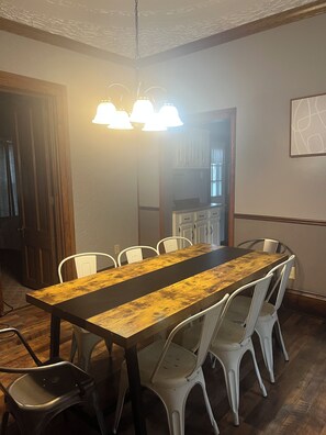 Un espace repas avec une longue table en bois, des chaises blanches et un luminaire suspendu.