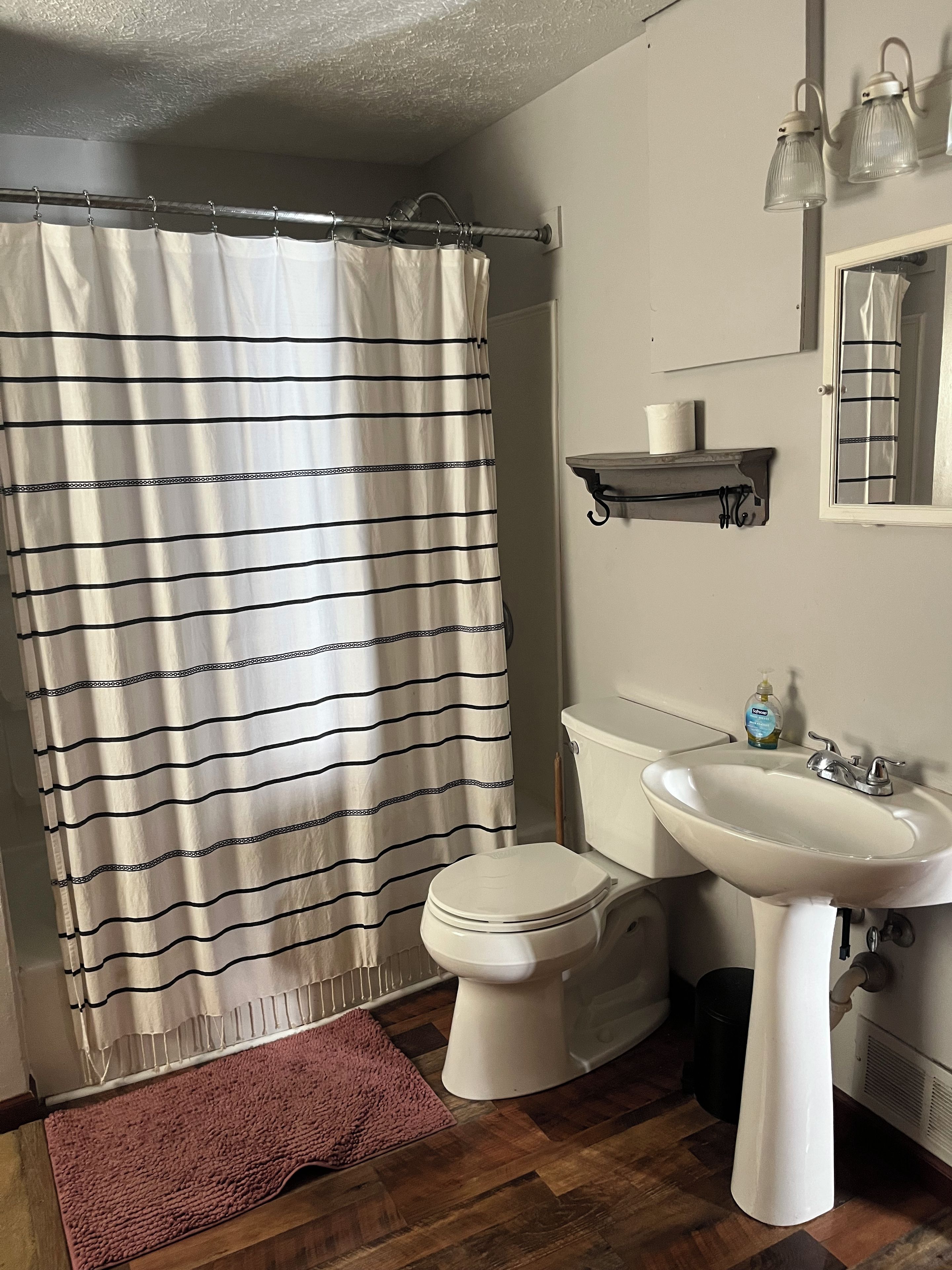 Une salle de bain équipée de toilettes, d’un lavabo, d’un rideau de douche et d’une petite étagère sur laquelle se trouve un rouleau de papier toilette.