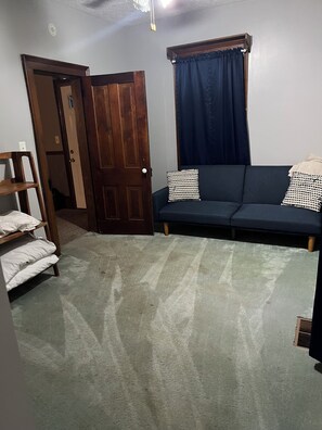 Une pièce avec un canapé bleu foncé, une porte en bois, un mur blanc et un tapis à motifs.