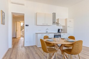 A modern kitchen with white cabinets, a central island, and a dining area with a wooden table and chairs. - 1-Bedroom Apartment with Air Conditioning | Landstraße | 4 Guests (Wien)