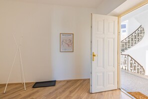 Quarto com porta branca, quadro pendurado na parede, abajur de chão branco e piso de madeira.