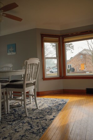 A room with a dining table, chairs, a large window, and a wooden floor. - The Little River Retreat - Riverfront (St. Clair)