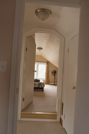 A hallway leading to a bedroom with a bed, a standing fan, and a window with curtains. - The Little River Retreat - Riverfront (St. Clair)