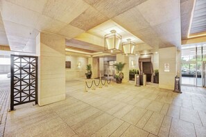 Eine geräumige Lobby mit Fliesenboden, einer Rezeption, Blumentöpfen und einem Sicherheitsposten.