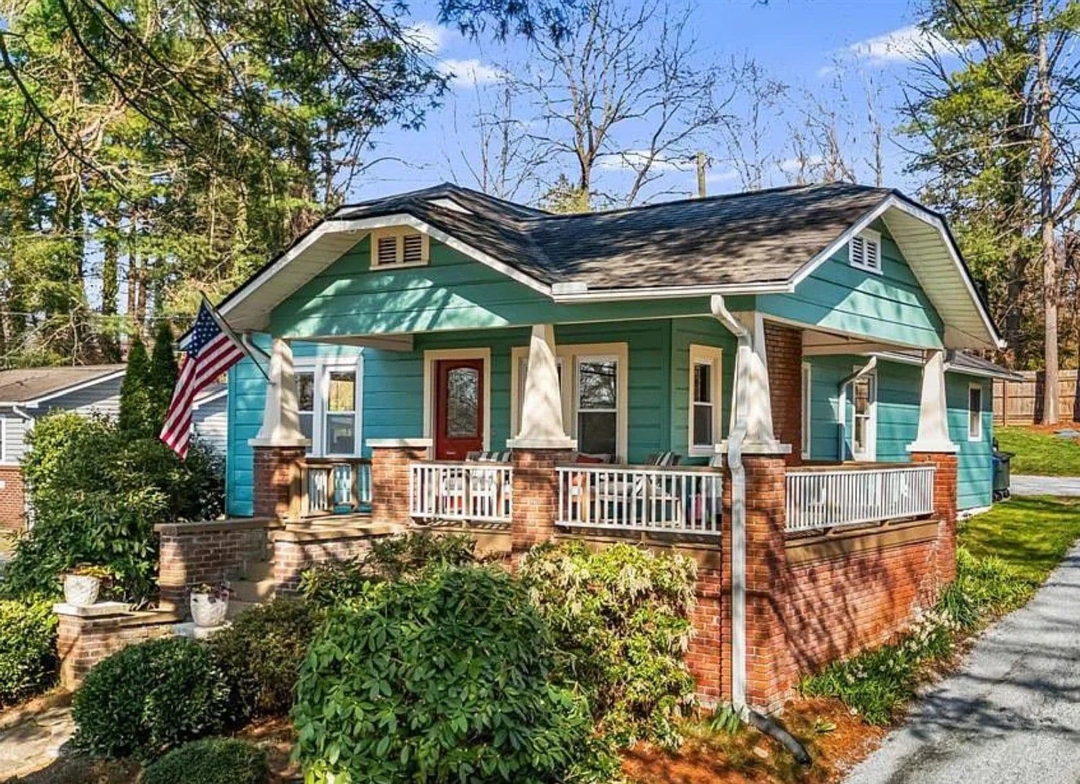 A two-story house with a front porch, a red door, and an American flag.