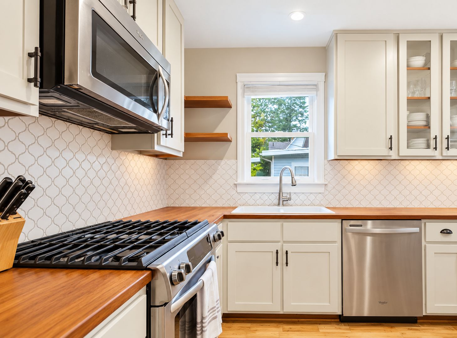 A modern kitchen with stainless steel appliances, white cabinetry, and a window providing natural light.