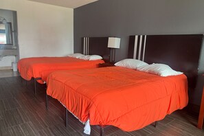 Hotellihuone, jossa on kaksi sänkyä, ja jokaisessa on punainen peitto ja valkoiset tyynyt.