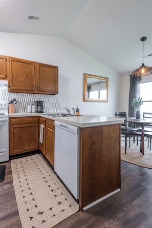 A modern kitchen with wooden cabinets, a built-in dishwasher, and a large island with a sink. - 1 bedroom Apartment 10 min from ECU (Greenville)