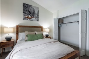 A bedroom with a bed, two bedside tables, a nightstand, a green throw pillow, a headboard, a wall-mounted lamp, a door, and a closet with a rod. - 1 bedroom Apartment 10 min from ECU (Greenville)