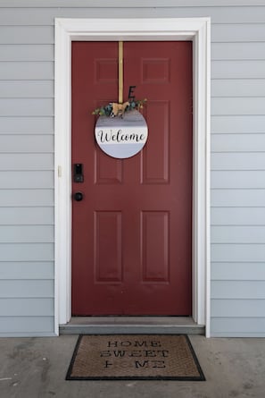 A red door with a 'Welcome' sign, a doormat, and a mailbox. - 1 bedroom Apartment 10 min from ECU (Greenville)