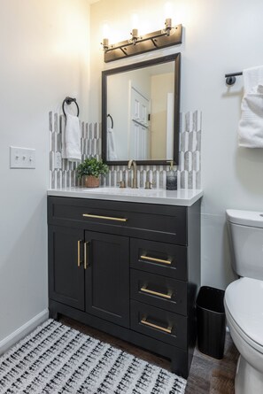 A bathroom with a dark vanity, a white sink, a mirror, and a toilet. - 1 bedroom Apartment 10 min from ECU (Greenville)