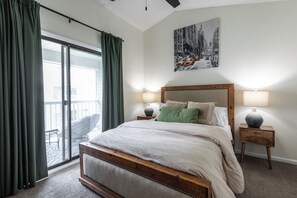 A bedroom with a large bed, two bedside lamps, a cityscape painting, and a sliding glass door. - 1 bedroom Apartment 10 min from ECU (Greenville)