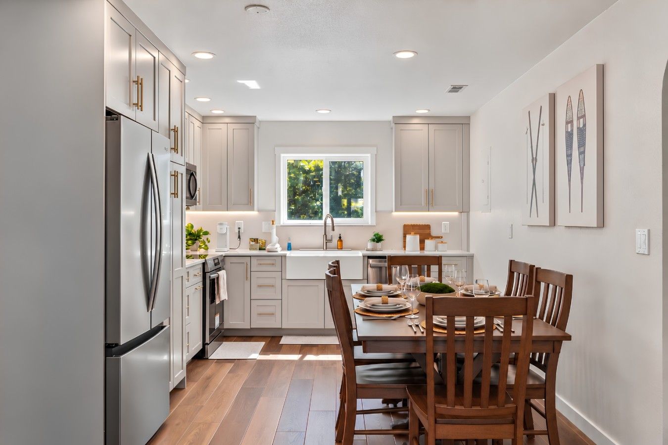 A modern kitchen with white cabinets, a stainless steel refrigerator, and a dining area with wooden chairs and a table set for four.