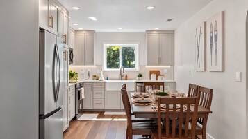 A modern kitchen with white cabinets, a stainless steel refrigerator, and a dining area with wooden chairs and a table set for four.