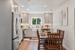 Una cocina moderna con gabinetes blancos, un refrigerador de acero inoxidable y un comedor con sillas de madera y una mesa para cuatro.