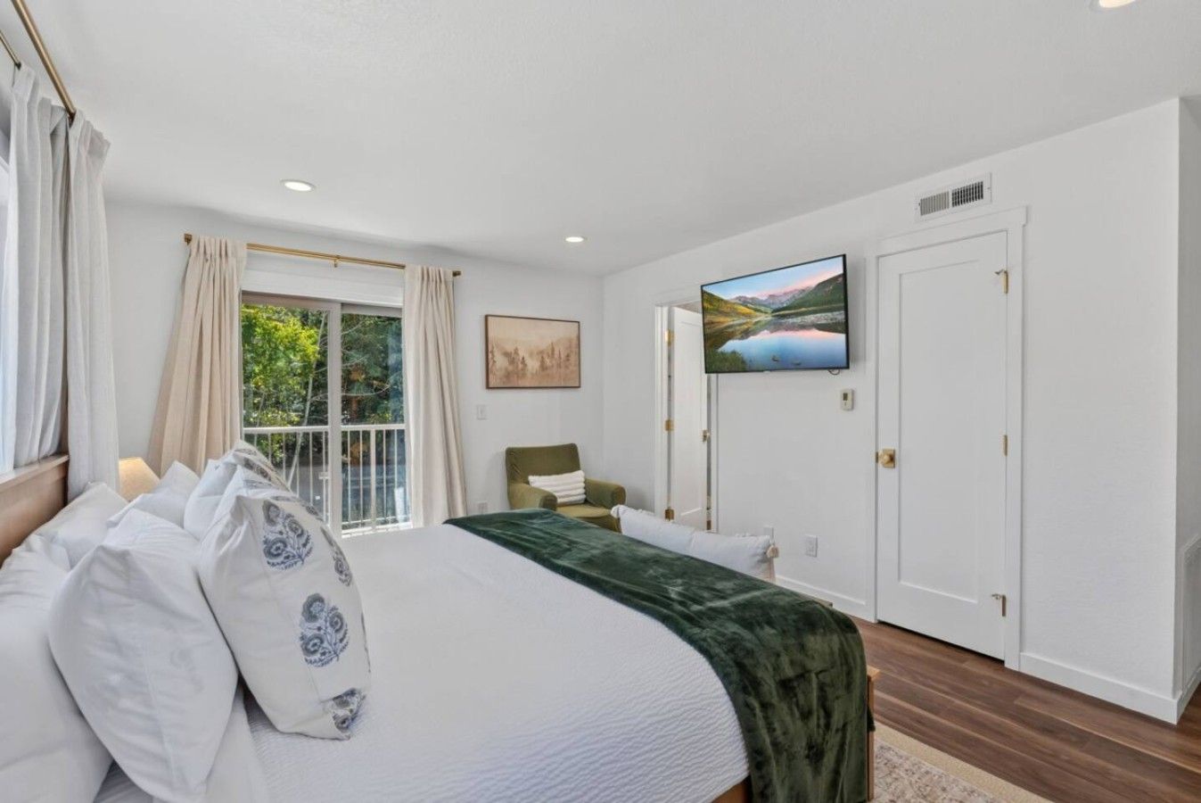 Un dormitorio con cama, televisor, silla y ventana con cortinas.