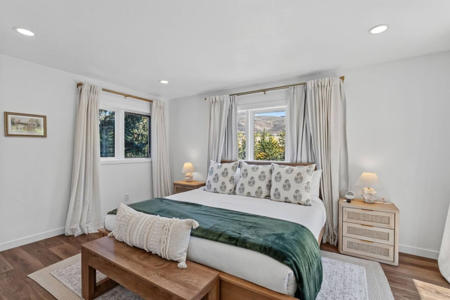 Un dormitorio con cama, mesitas de noche, un banco y cortinas.