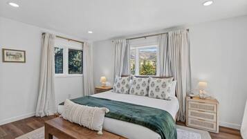 Un dormitorio con cama, mesitas de noche, un banco y cortinas.