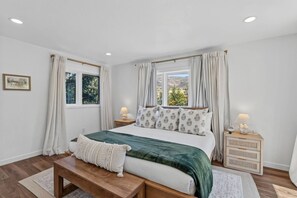 Ein Schlafzimmer mit einem Bett, Nachttischen, einer Bank und Vorhängen.