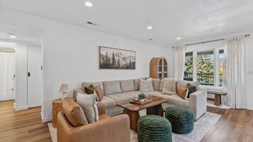 A modern living room with a sectional sofa, a coffee table, and a large window with curtains.