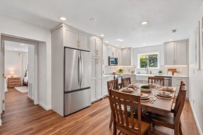 Una cocina moderna con armarios blancos, un refrigerador de acero inoxidable y un comedor con sillas de madera y una mesa preparada para cuatro.