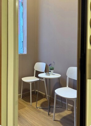A small room with two white chairs and a round table, a potted plant on the table, and a window with a view of buildings. - A comfortable duplex in Fresku, Tirana. (Tiranë)